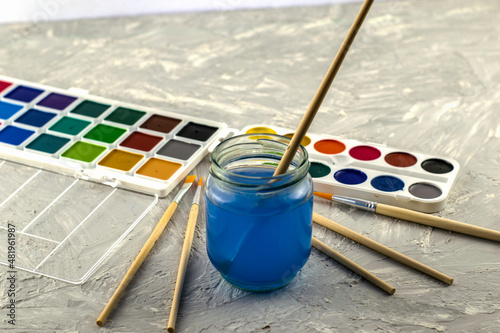 watercolor paints a jar of water and brushes for drawing on a gray textured surface