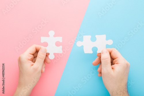 Canvastavla Young adult man and woman hands holding and putting together white puzzle pieces on light pink blue table background