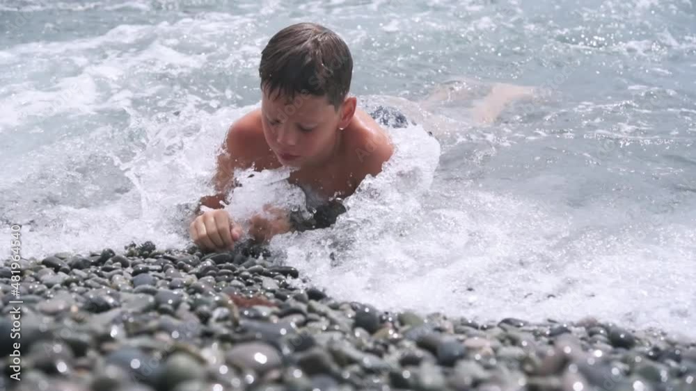 A boy lying on the pebbe beach with foamy sea waves hitting the pebble seashore behind him A boy lying on the pebbe beach with foamy sea waves hitting the pebble seashore behind him