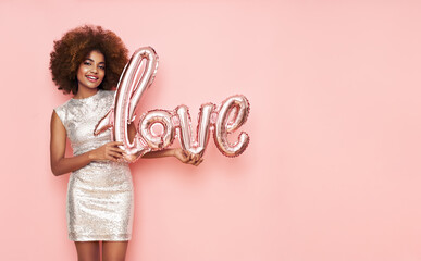 A beautiful young African-American woman with a balloon in the shape of the inscription love on a pink background. Woman on Valentine's Day. Symbol of love