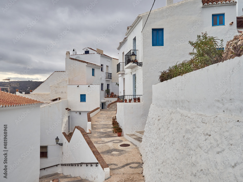 Typical street of Frigiliana, a small white village with cobblestone streets in the  Axarquía region of the Costa del Sol, Málaga province, Andalusia, Spain. White houses with blue windows