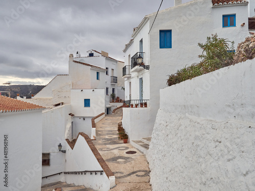Fototapeta Naklejka Na Ścianę i Meble -  Typical street of Frigiliana, a small white village with cobblestone streets in the  Axarquía region of the Costa del Sol, Málaga province, Andalusia, Spain. White houses with blue windows