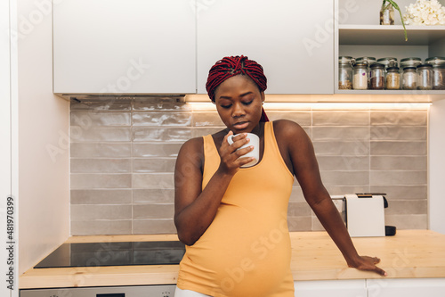black pregnant woman taking a cup of coffee at the kitchen