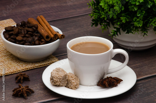 Fragrant coffee in a small coffee cup with cane sugar and spices in the form of anise and cinnamon on a wooden table.