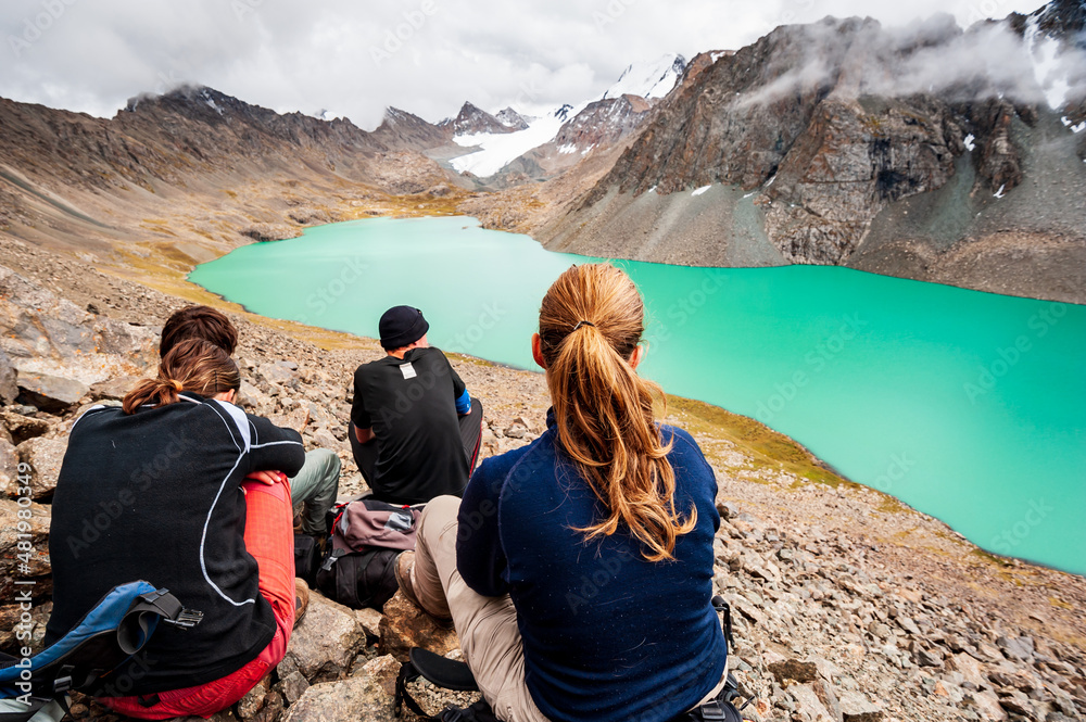 Fototapeta premium Group of trekker backpackers sitting relaxing at bank of Beautiful landscape of turquoise Ala-Kul Lake, Karakol valley, Issyk-kul region, Ala-kul lake Terskey Alatau range, Kyrgyzstan, Central Asia.