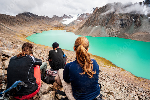 Group of trekker backpackers sitting relaxing at bank of Beautiful landscape of turquoise Ala-Kul Lake, Karakol valley, Issyk-kul region, Ala-kul lake Terskey Alatau range, Kyrgyzstan, Central Asia.