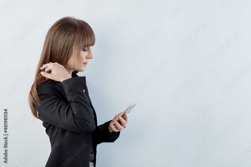 Business portrait of woman with phone - happy young white businesswoman in business casual standing against gray wall. Copy space for text. Business portrait of woman with phone - happy young white businesswoman in business casual standing against gray wall. Copy space for text.