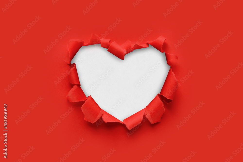 A paper hole with torn edges on a red background. Through paper. A ragged hole in the shape of a heart. Valentine's day. A symbol of love, romantic relationships. International Women's Day. - obrazy, fototapety, plakaty 