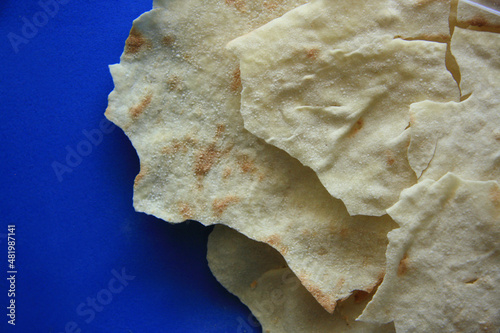 Traditional Sardinian bread, Italian speciality food. Close-up of Carasau Bread. Focaccia, rustic crispy pastry on a blue background.