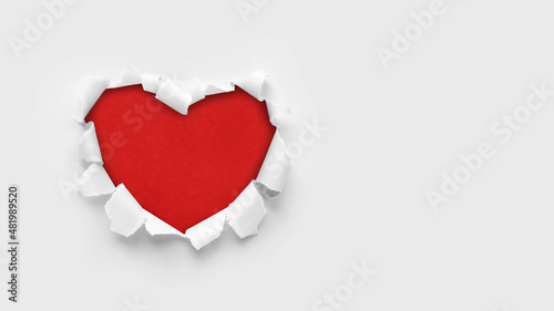 A paper hole with torn edges on a white background. Through paper. A ragged hole in the shape of a heart. Valentine's day. A symbol of love, romantic relationships. International Women's Day.