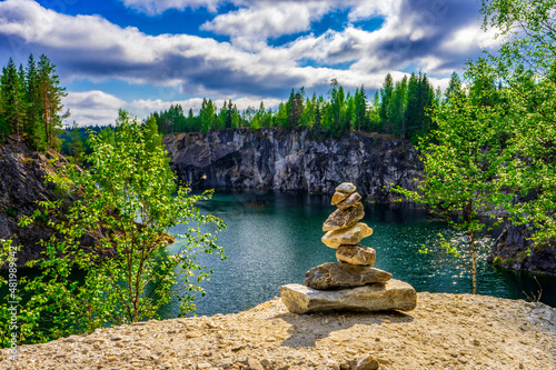 Stacked stones or obo against wonderful landscape of quarry with turquoise water in northern forest on summer day. Beautiful scene, nature of russian north. Ruskeala marble canyon, Karelia, Russia