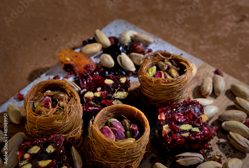 sweets with pistachios and dried fruits in baskets laid out on a wooden board on a brown background © Mariyka LnT