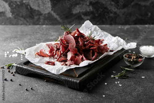 Cuadro en lienzo Board with spicy beef jerky on dark background
