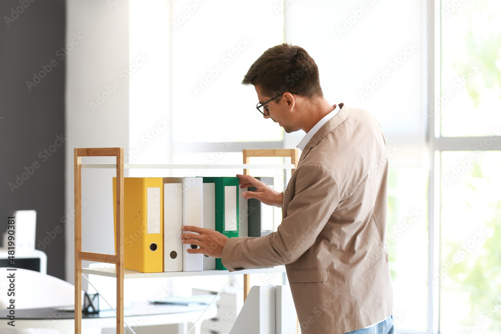 Young man taking folder from shelf in office