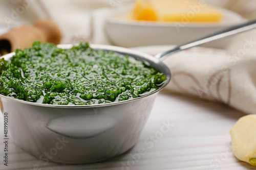 Pot of tasty pesto sauce and ingredients on light wooden background