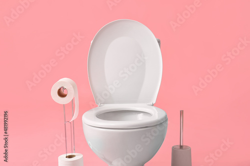 Holder with rolls of paper, toilet bowl and brush on color background, closeup