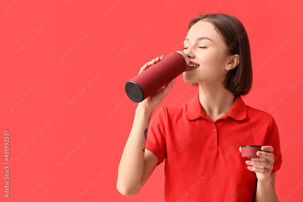 Beautiful young woman drinking hot tea from thermos on color background Beautiful young woman drinking hot tea from thermos on color background