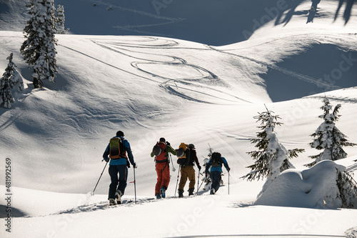Ski tour group of people with ski equipment walks along winter snowy path to mountain slope