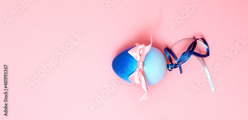 One blue plastic egg with satin ribbons and bow on pink background. Easter card with holiday symbol and place for text. Mock up design with copy space. Handmade decoration. DIY. One thing. Cute gift