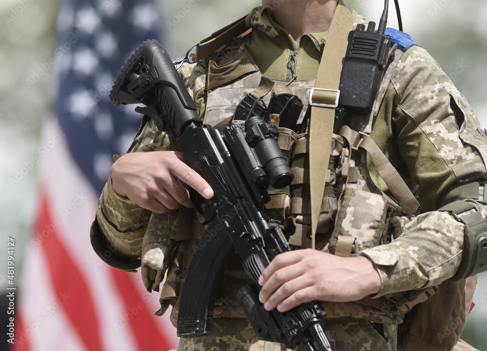 Soldier with assault rifle and US flag at the background. US military support Ukraine. Soldier with assault rifle and US flag at the background. US military support Ukraine.