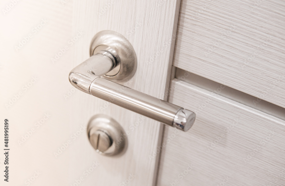 Metallic chrome handle on white wooden interior door. Modern door handle.
