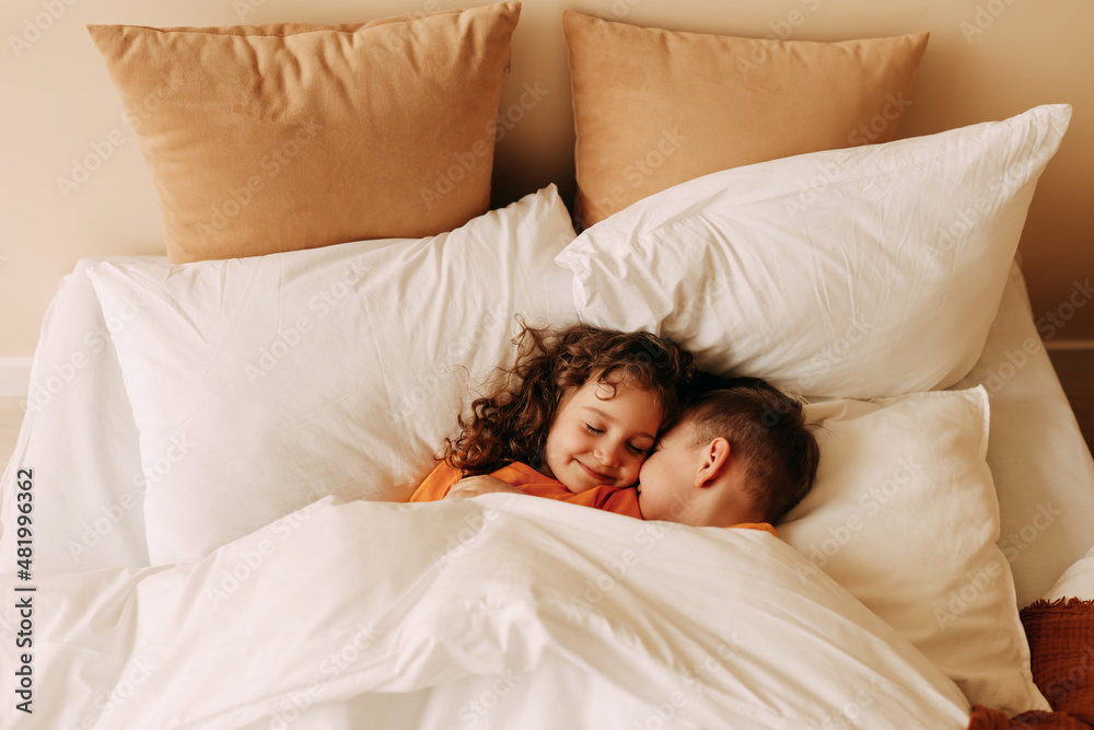 Smiling funny twin children a little boy and a girl in pajamas sleep together lying on pillows on the bed in a cozy comfortable bedroom. Top view. Selective focus