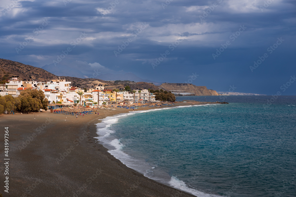 Wide sandy beach and Mediterranean town by the sea under dramatic clouds, Myrtos, Crete, Greece