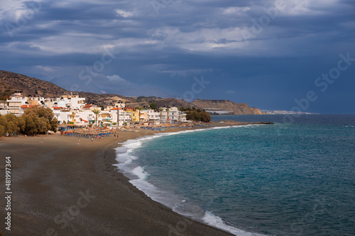 Wide sandy beach and Mediterranean town by the sea under dramatic clouds, Myrtos, Crete, Greece