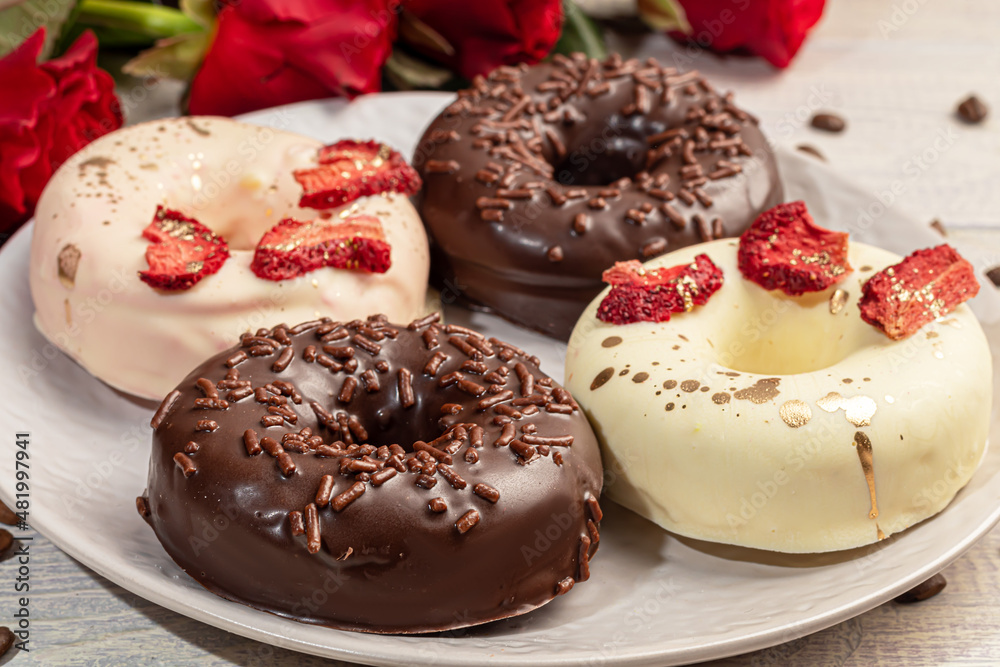 Handmade donuts on a light background in white and black chocolate. There are flowers nearby. Women's day, Valentine's day. Handmade donuts on a light background in white and black chocolate. There are flowers nearby. Women's day, Valentine's day.