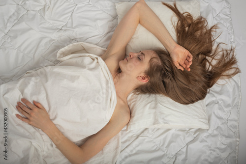 Beautiful young woman with long hair sleeps soundly on expensive bed linen. Portrait of sleeping girl top view.