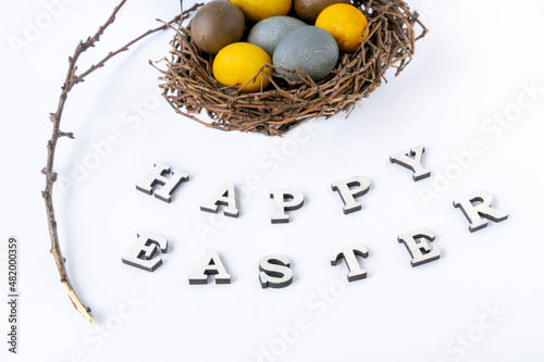 Multicolored eggs in birds nest, branch and the inscription Happy easter on white background.