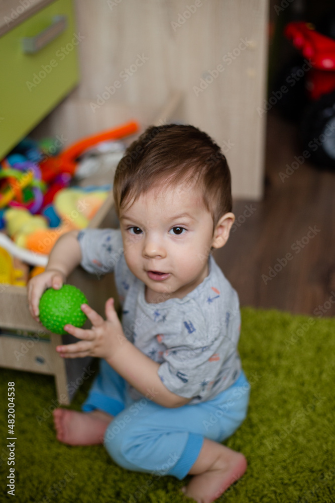 Fototapeta premium child toddler playing toys at home or nursery, baby holds a green ball in his hand