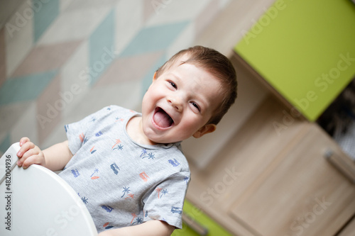Handsome baby laughs and looks at the camera, baby is holding on to the high chair