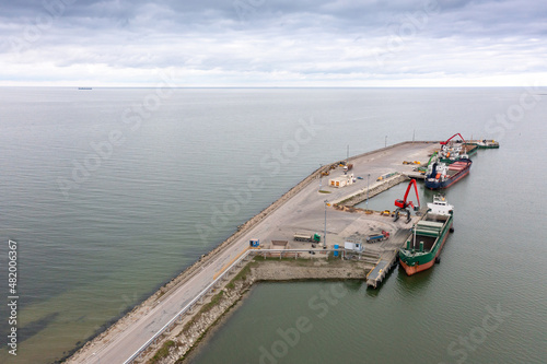 An aerial drone view of the industrial port in the Baltic Sea. There is a ships under load in the harbor. 