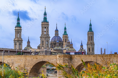 Foto Medieval stone bridge Puente de Piedra with arches on the background of the belltowers of the Basilica of Our Lady of the Pillar in Saragossa