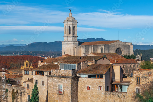 Girona Cathedral rises above the tiled roofs of the Gothic Quarter in the Old Town. Medieval cityscape with ancient buildings against the backdrop of mountains and blue sky on a sunny autumn day