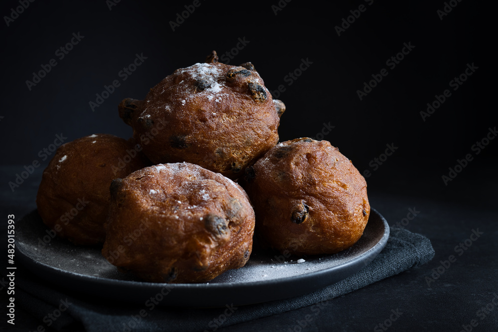 Deep-fried raisins buns. Dutch donuts with raisins and powdered sugar on a plate. Dark moody food photography style with selective focus and copy space, horizontal