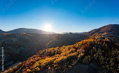 Bright sunrise at high mountains covered with autumn forest