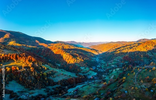 Shaded mountain valley with houses and forests at sunset