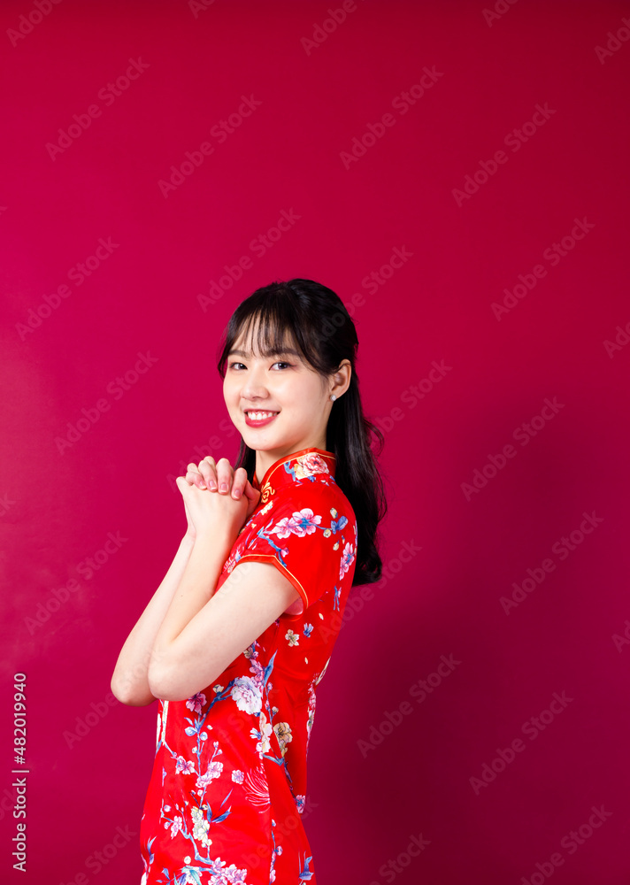 Smiling asian young woman in traditinal red cheongsam dress pointing hand to empty space on red background. Smiling asian young woman in traditinal red cheongsam dress pointing hand to empty space on red background.