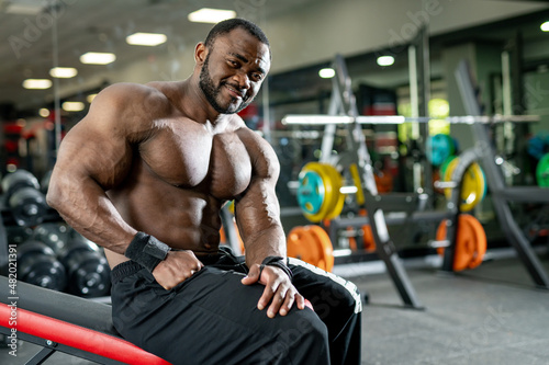 Muscular shirtless bodybuilder smiling into camera. Portrait of attractive athletic sportsman in gym.