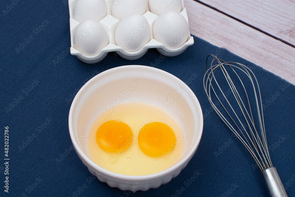 Egg preparation for recipe, with broken eggs, egg tray and a fouet on a blue towel and a wooden table, top view Egg preparation for recipe, with broken eggs, egg tray and a fouet on a blue towel and a wooden table, top view