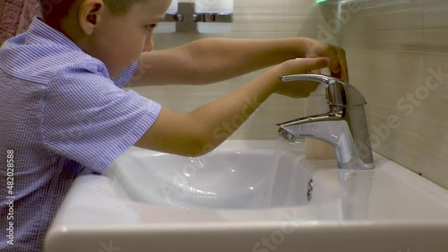 a boy in a shirt washes his hands with liquid soap in the bathroom