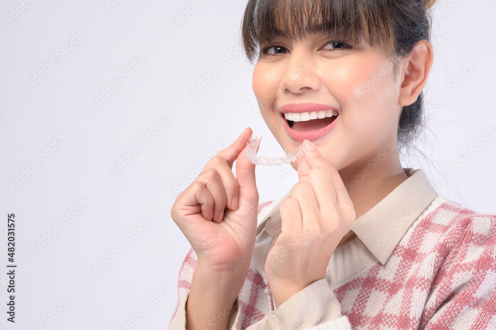 Young smiling woman holding invisalign braces over white background studio, dental healthcare and Orthodontic concept. Young smiling woman holding invisalign braces over white background studio, dental healthcare and Orthodontic concept.