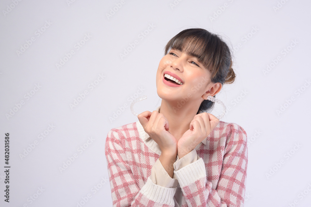 Young smiling woman holding invisalign braces over white background studio, dental healthcare and Orthodontic concept. Young smiling woman holding invisalign braces over white background studio, dental healthcare and Orthodontic concept.