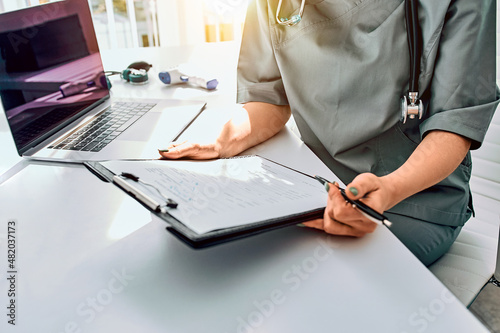 Cropped image of a doctor woman dressed in a medical suit in the office holding a form.