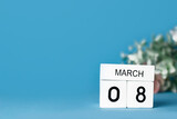 Calendar with white wooden date made from cubes. March 8. International Women's Day. Blue background and a bouquet .