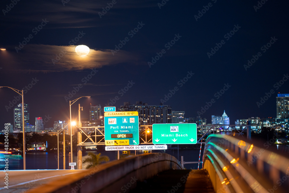 Night photo bridge to Miami Beach. road signs and moon in the sky