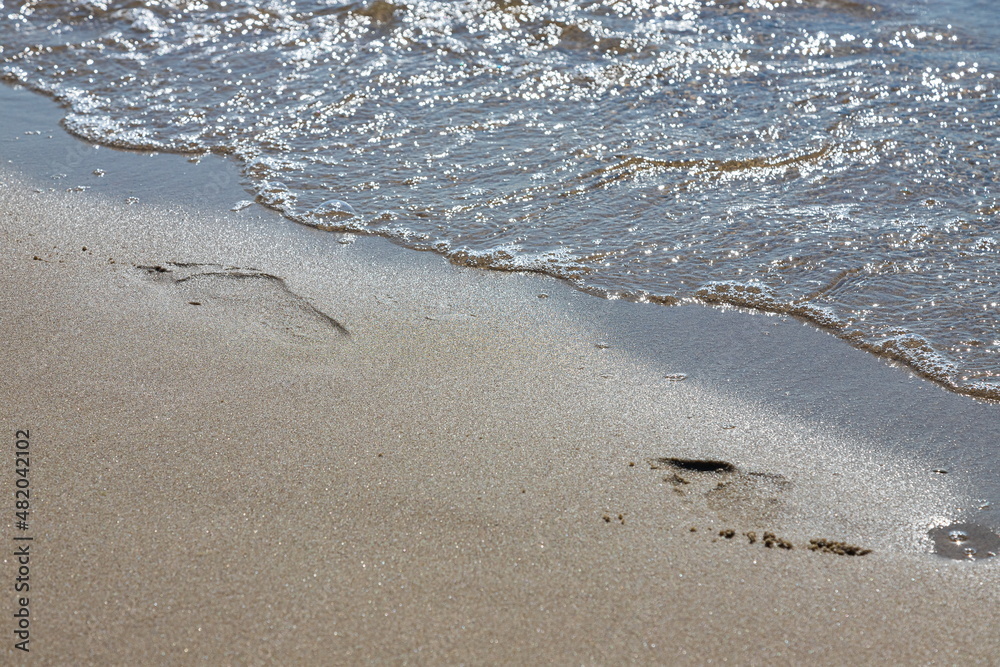 Footprints of a man on the yellow beach sand from walking barefoot by the sea with water that washes away the footprints. Footprints of a man on the yellow beach sand from walking barefoot by the sea with water that washes away the footprints.