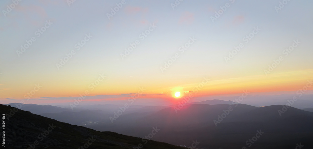 Colorful sun setting over peaks looking out from the Appalachian Trail on Mt. Washington, White Mountains, New Hampshire, mountains in silhouette.  Suitable for background, with copy space.